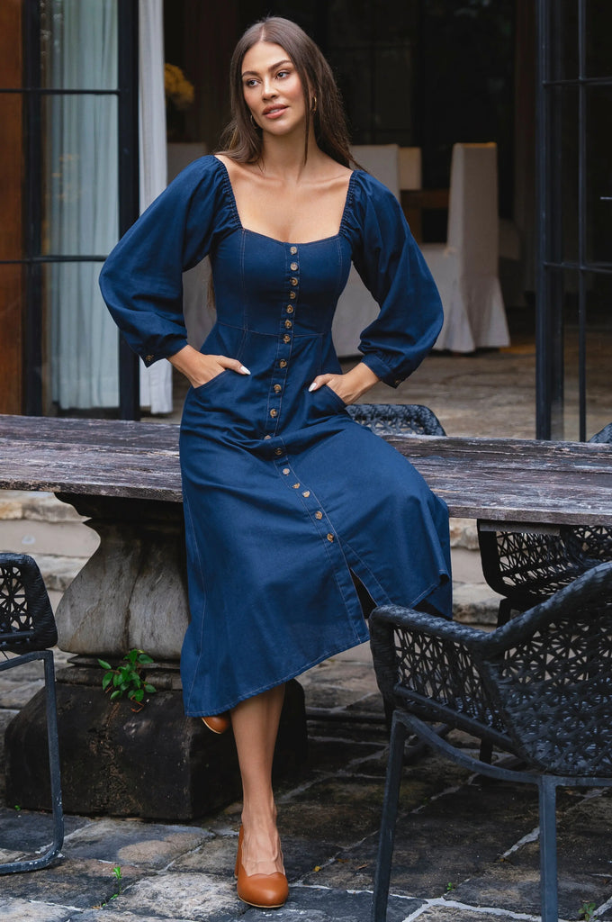 Woman in a blue dress standing outdoors on a patio.