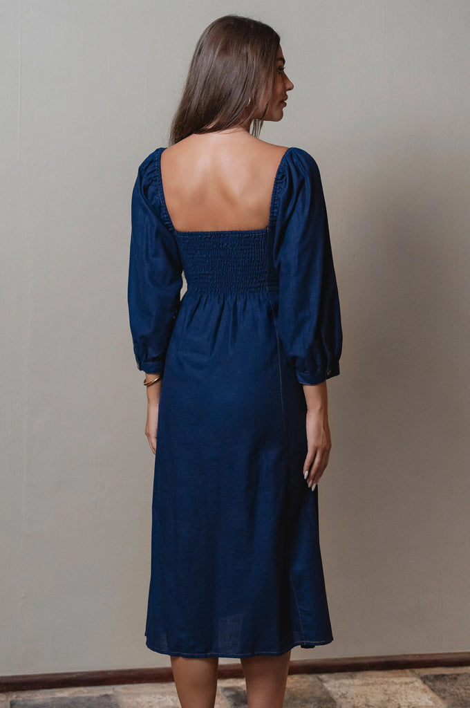 Woman wearing a blue dress with long sleeves and an open back against a plain background