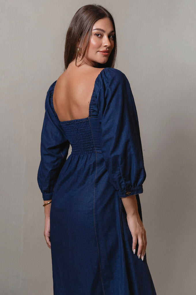 Woman wearing a blue dress with long sleeves and an open back against a neutral background