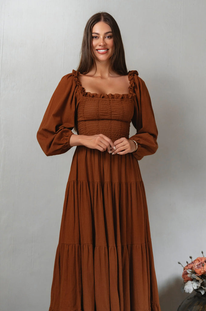 Woman wearing a brown smocked midi dress against a plain background