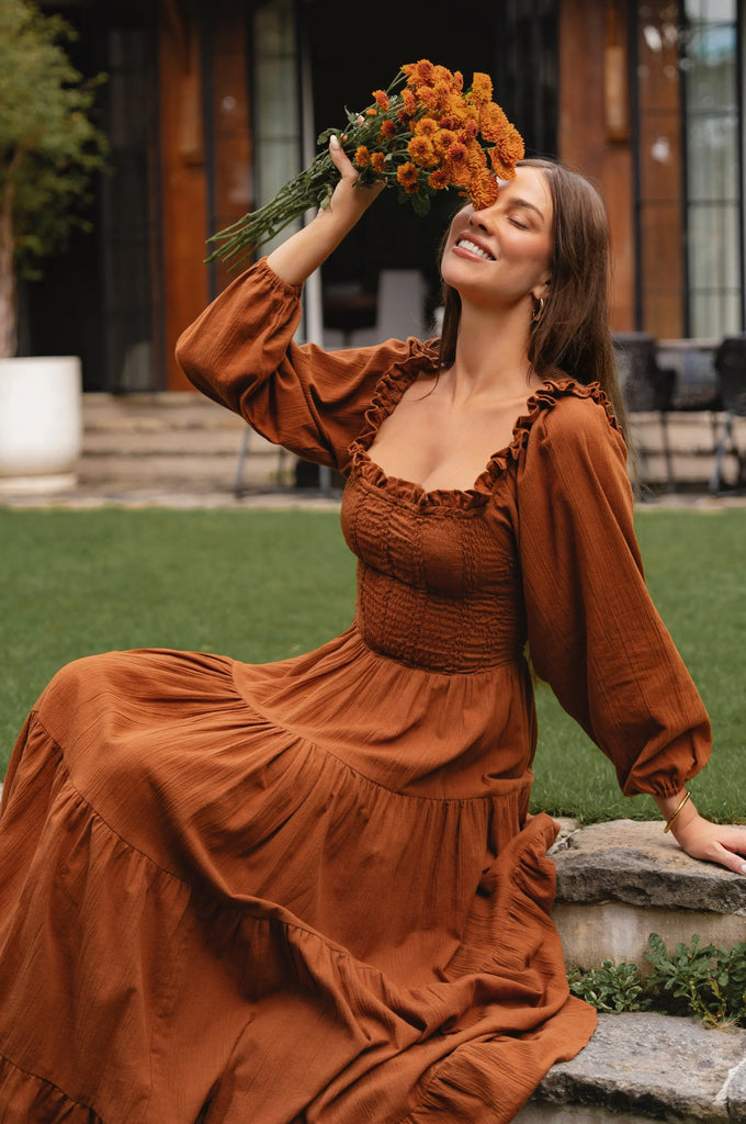 Woman in a brown long sleeve dress holding flowers outdoors country style