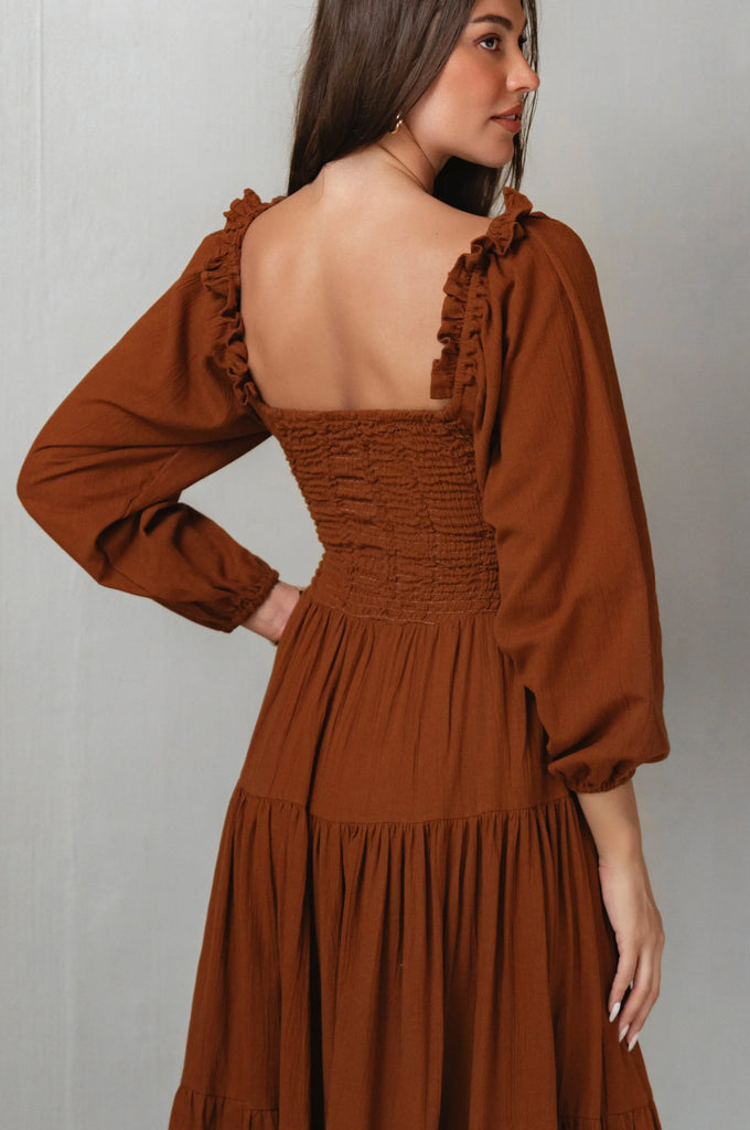 Brown dress with long sleeves and ruffled details on a plain background