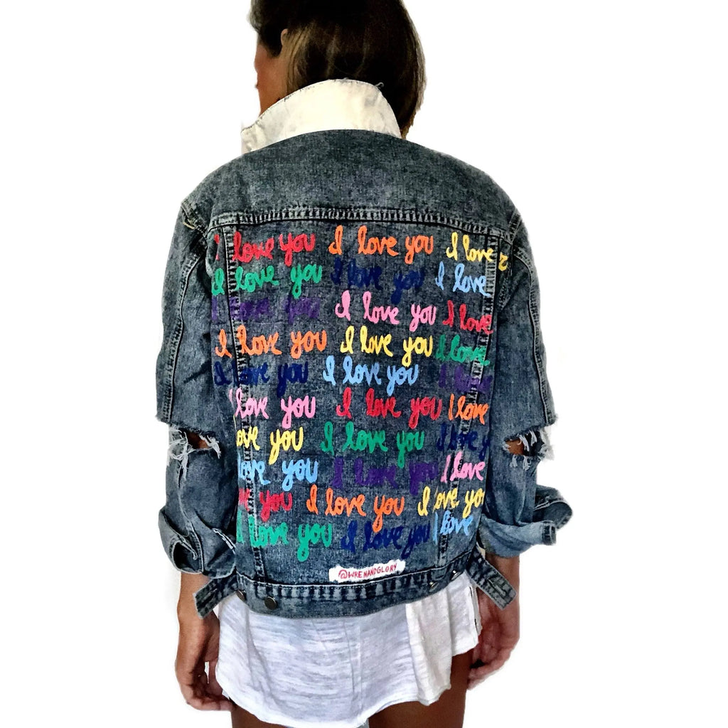 Medium blue denim wash. 'I Love You' painted in rainbow cursive, over and over. White painted pockets and collar, with dripping heart on arm. Signed @wrenandglory.