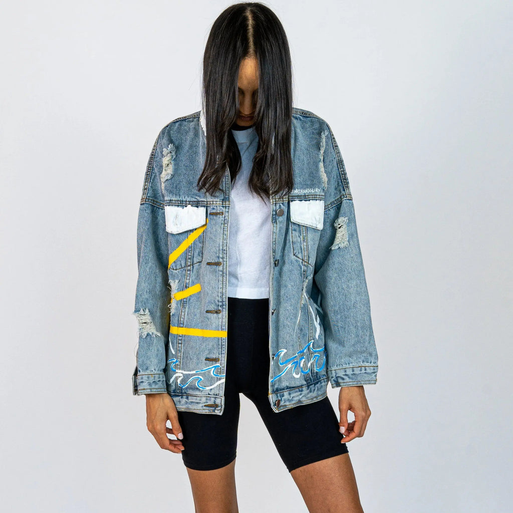 Lighter blue denim wash. Outline of mountain range, ocean waves, and sun setting surrounding entire jacket. Collar and front pockets painted white. Signed @wrenandglory.