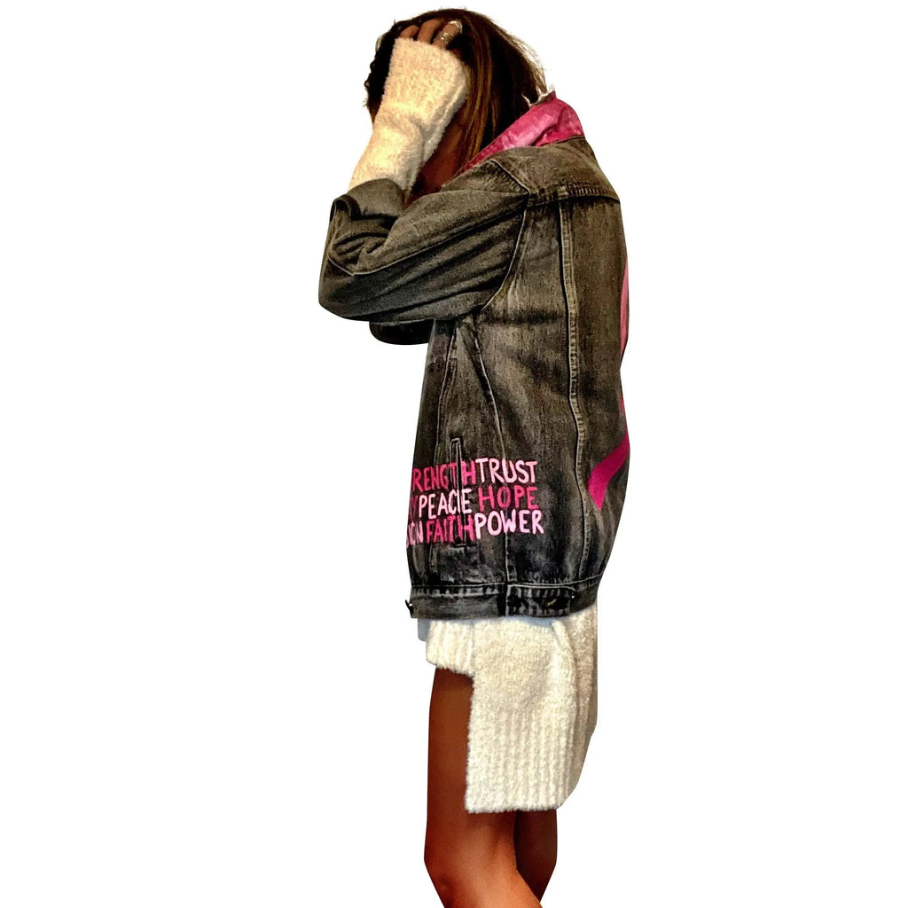 Faded black denim. Pink ombre Breast Cancer ribbon painted in large on back. Love, Strength, Trust, Beauty, Peace, Hope, Passion, Faith, Power painted in light & bright pink on the front. Collar painted in pink ombre. Signed @wrenandglory.