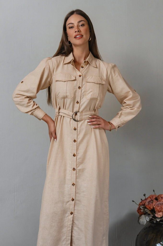 Woman wearing a beige dress with a belt against a gray background