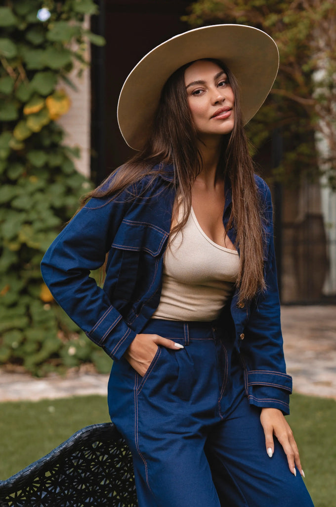 Woman wearing a blue denim outfit with a beige hat in an outdoor setting