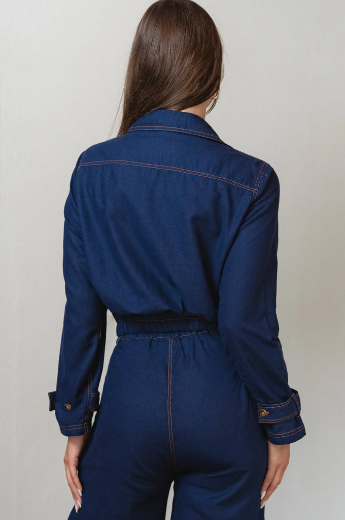 Person wearing a blue denim jacket and pants against a plain background