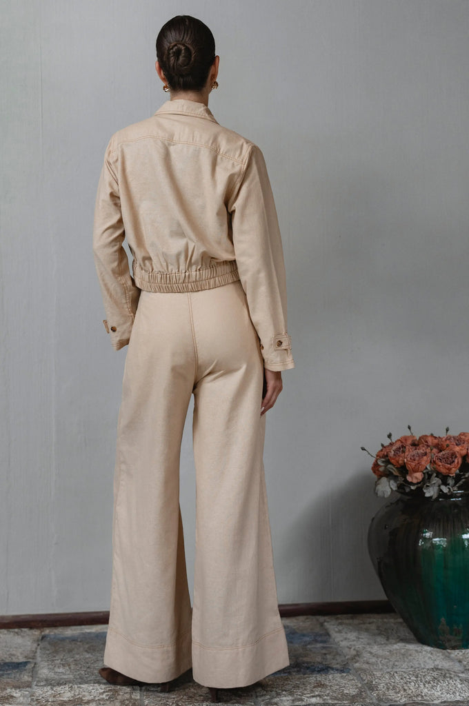 Person wearing a beige jacket and pants standing against a plain wall - cottage core style