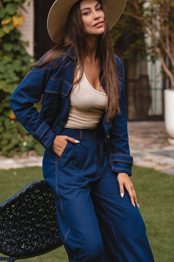 Woman in a navy linen denim like outfit with a beige hat standing outdoors.