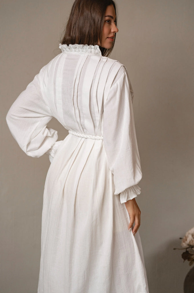 Woman wearing a white linen dress with long sleeves against a plain background