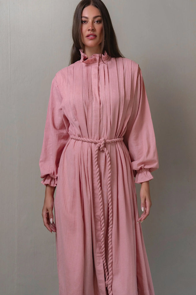 Woman wearing a pink dress with long sleeves against a gray background